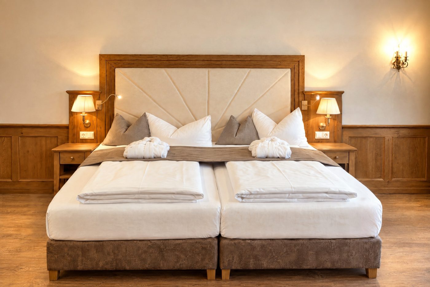 Doppelbett mit gepolstertem Kopfteil vor der Holzvertäfelung in einer vergleichbaren Deluxe-Suite vom Typ des Zimmers Elias im Hotel DreiSonnen in Serfaus