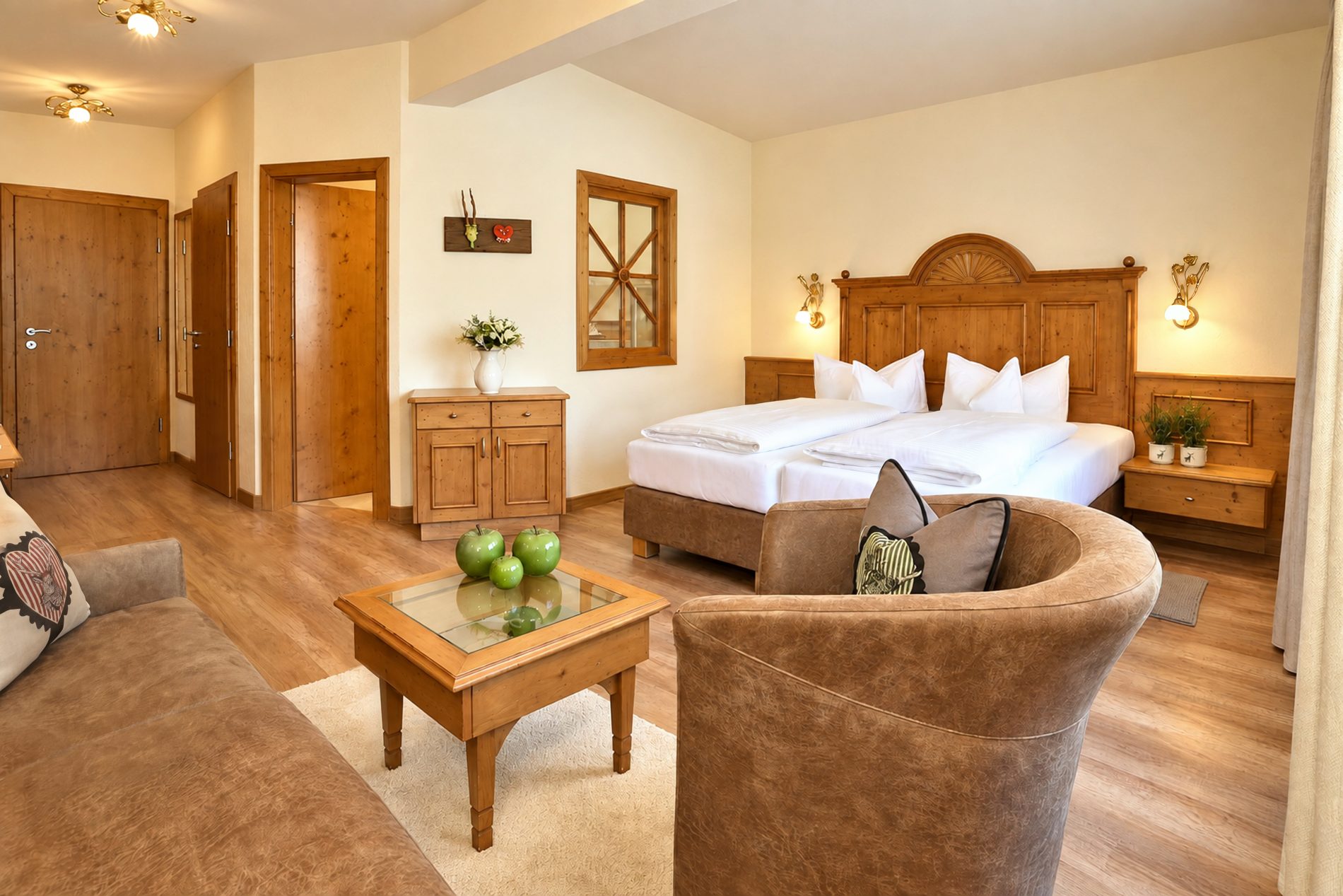 Doppelbett mit geschnitztem Kopfteil, Kommode und Sitzgruppe mit Sessel und Couchtisch in einem vergleichbaren Zimmer vom Typ der Suite Elisabeth im Hotel DreiSonnen in Serfaus
