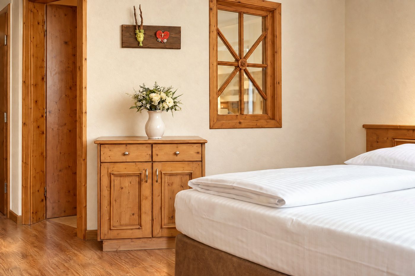 Holzkommode mit Blumenvase unter einem Sprossenfenster in einem vergleichbaren Zimmer vom Typ der Suite Elisabeth im Hotel DreiSonnen in Serfaus