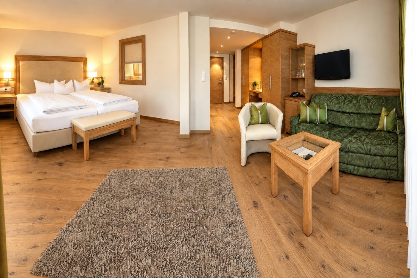 Doppelbett, grünes Sofa und TV in einem vergleichbaren Zimmer vom Typ der Suite Elisabeth im Hotel DreiSonnen in Serfaus