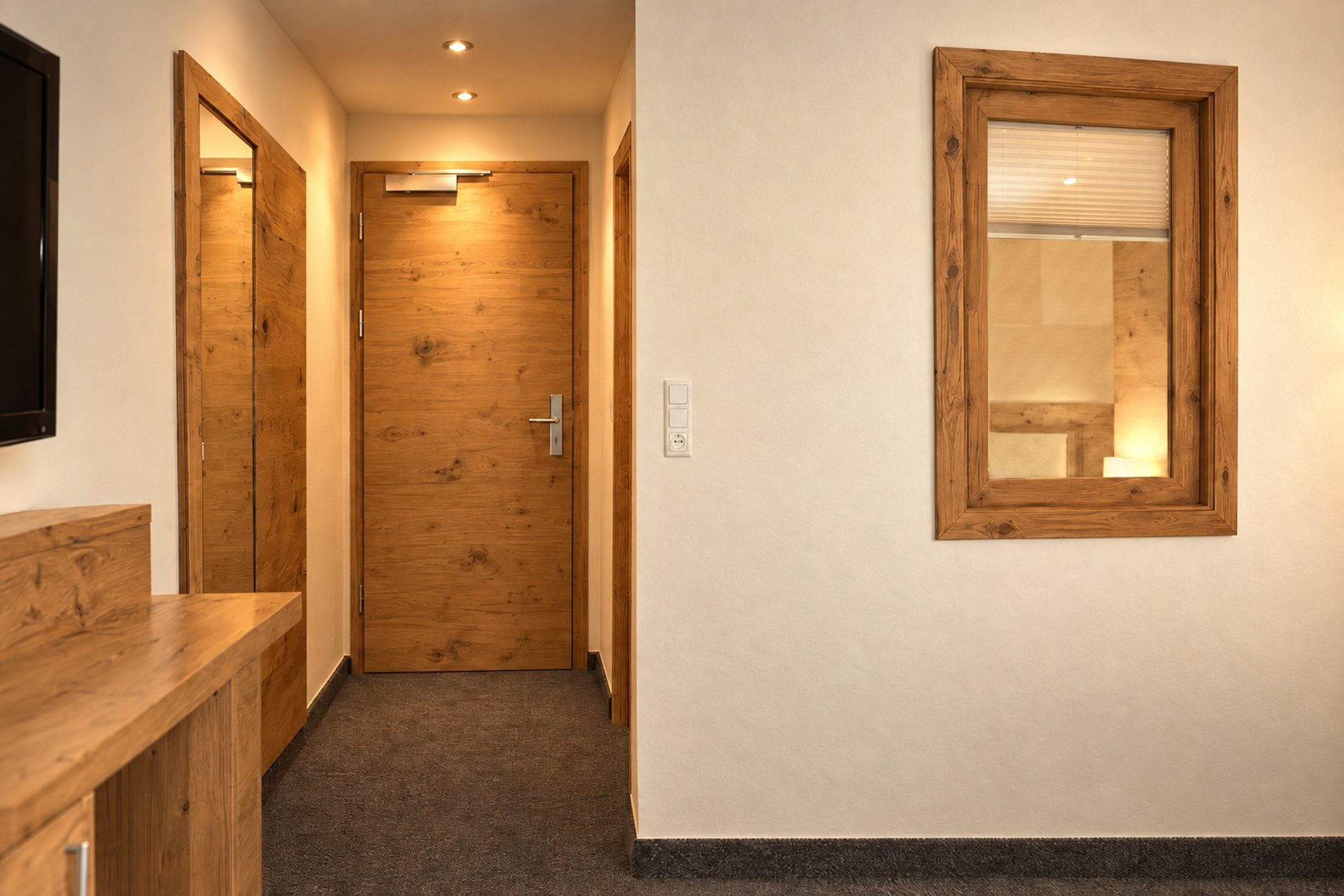 Entrance area with wooden door, cloakroom and interior window to the bathroom in the room Florian at Hotel DreiSonnen in Serfaus