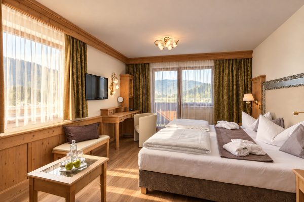 Bed, bench, desk and balcony door with mountain views in the Family Room Kaiser Franzl at Hotel DreiSonnen in Serfaus