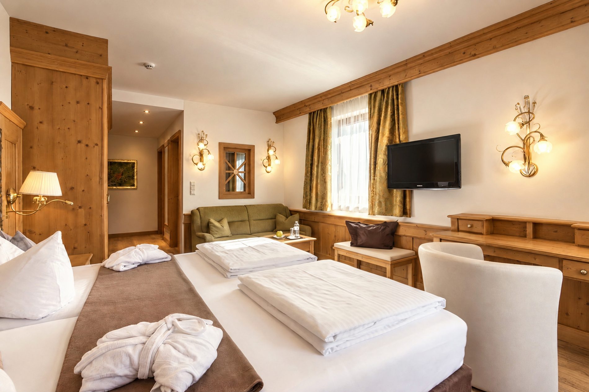 Bed looking towards the green sofa, television and wooden wardrobe in the Kaiser Franzl room at Hotel DreiSonnen in Serfaus