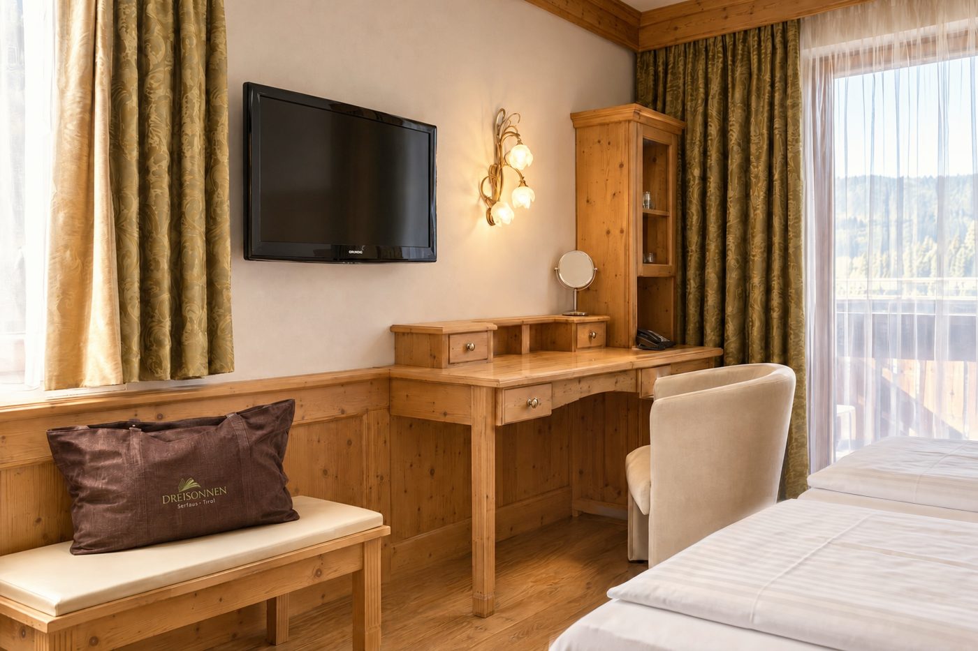 Desk with television, armchair and bench with spa bag in the Kaiser Franzl room at Hotel DreiSonnen in Serfaus