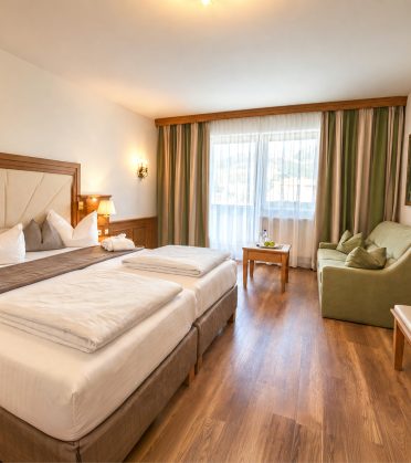 Komfort-Doppelzimmer Jonas im Hotel DreiSonnen in Serfaus mit Doppelbett, grünem Sofa und Fenster mit Bergblick