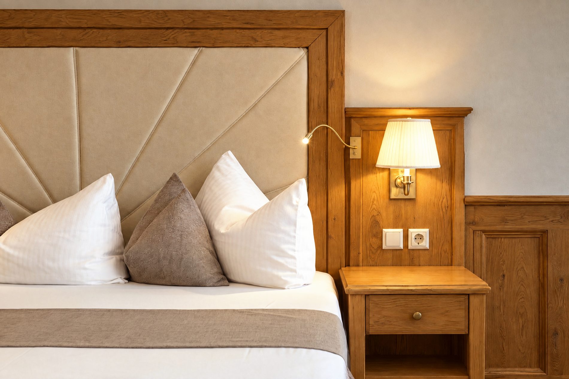 Nachttisch mit Wandleuchte und Leselampe neben dem gepolsterten Kopfteil im Zimmer Jonas des Hotels DreiSonnen in Serfaus