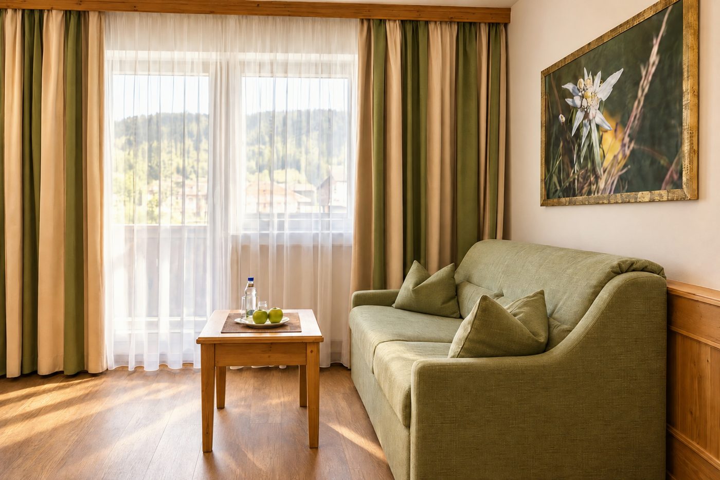 Grünes Sofa mit Beistelltisch und Edelweißbild vor dem Fenster mit Blick ins Grüne im Zimmer Jonas des Hotels DreiSonnen in Serfaus