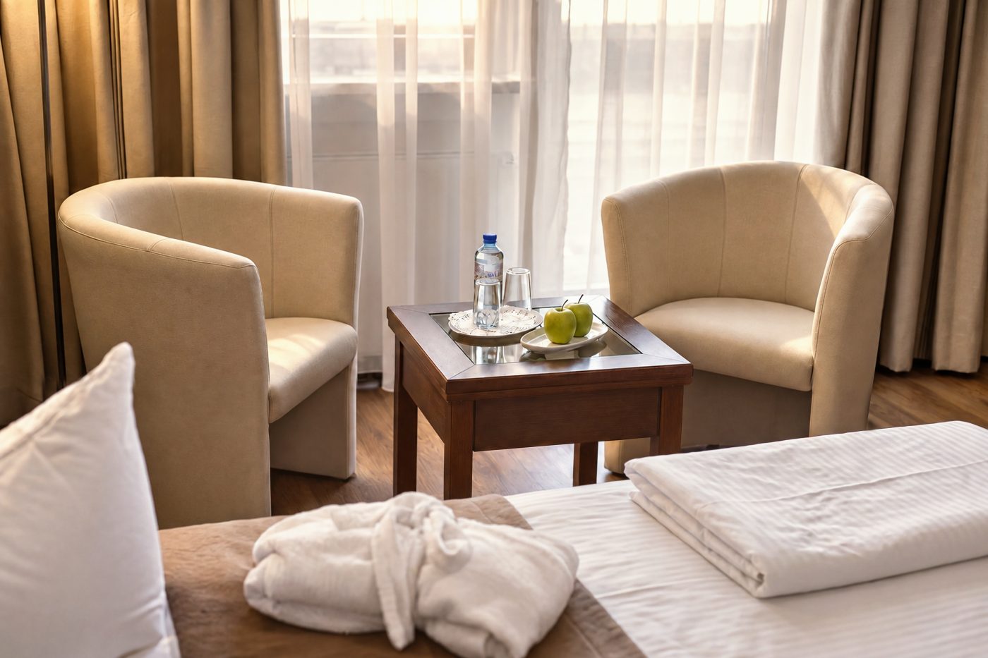 Zwei Sessel mit Beistelltisch, Wasser und Äpfeln am Fenster in einem vergleichbaren Komfort-Doppelzimmer vom Typ des Zimmers Jonas im Hotel DreiSonnen in Serfaus