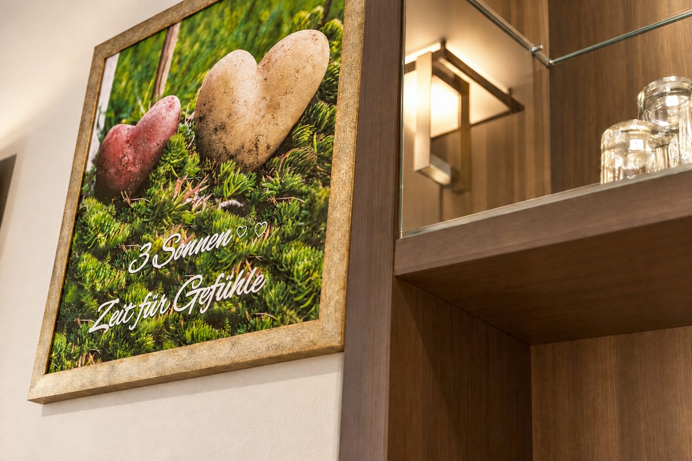 Wandbild mit zwei herzförmigen Steinen neben einem beleuchteten Regal in einem vergleichbaren Komfort-Doppelzimmer vom Typ des Zimmers Jonas im Hotel DreiSonnen in Serfaus