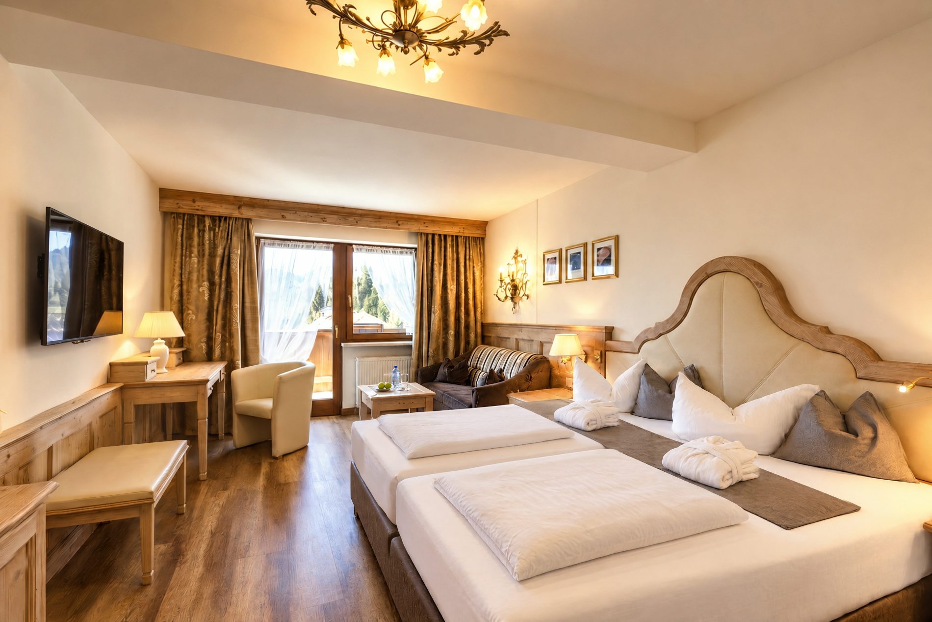 Doppelbett mit geschwungenem Kopfteil, Sitzecke und Balkontür mit Blick ins Grüne im Deluxe-Doppelzimmer Kaiserin Sissi des Hotels DreiSonnen in Serfaus