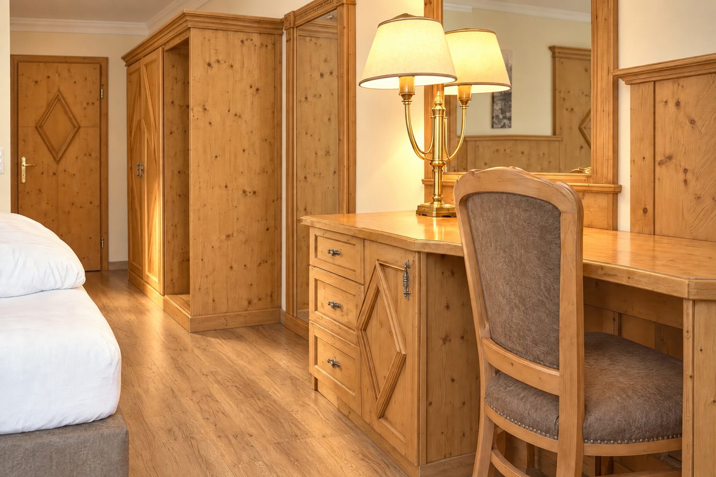 Schreibtisch mit Stuhl, Spiegel und Kleiderschrank aus Holz im Zimmer König Ludwig des Hotels DreiSonnen in Serfaus