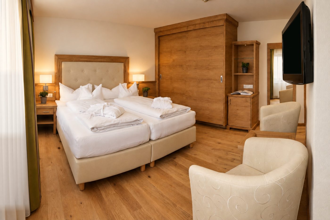 Doppelbett, Schiebetürschrank und zwei Sessel in einem vergleichbaren Komfort-Einzelzimmer vom Typ des Zimmers König Ludwig im Hotel DreiSonnen in Serfaus