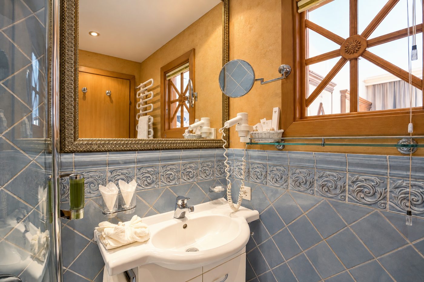 Badezimmer im Zimmer König Ludwig des Hotels DreiSonnen in Serfaus mit Waschtisch, Spiegel, blauen Reliefkacheln und Sprossenfenster