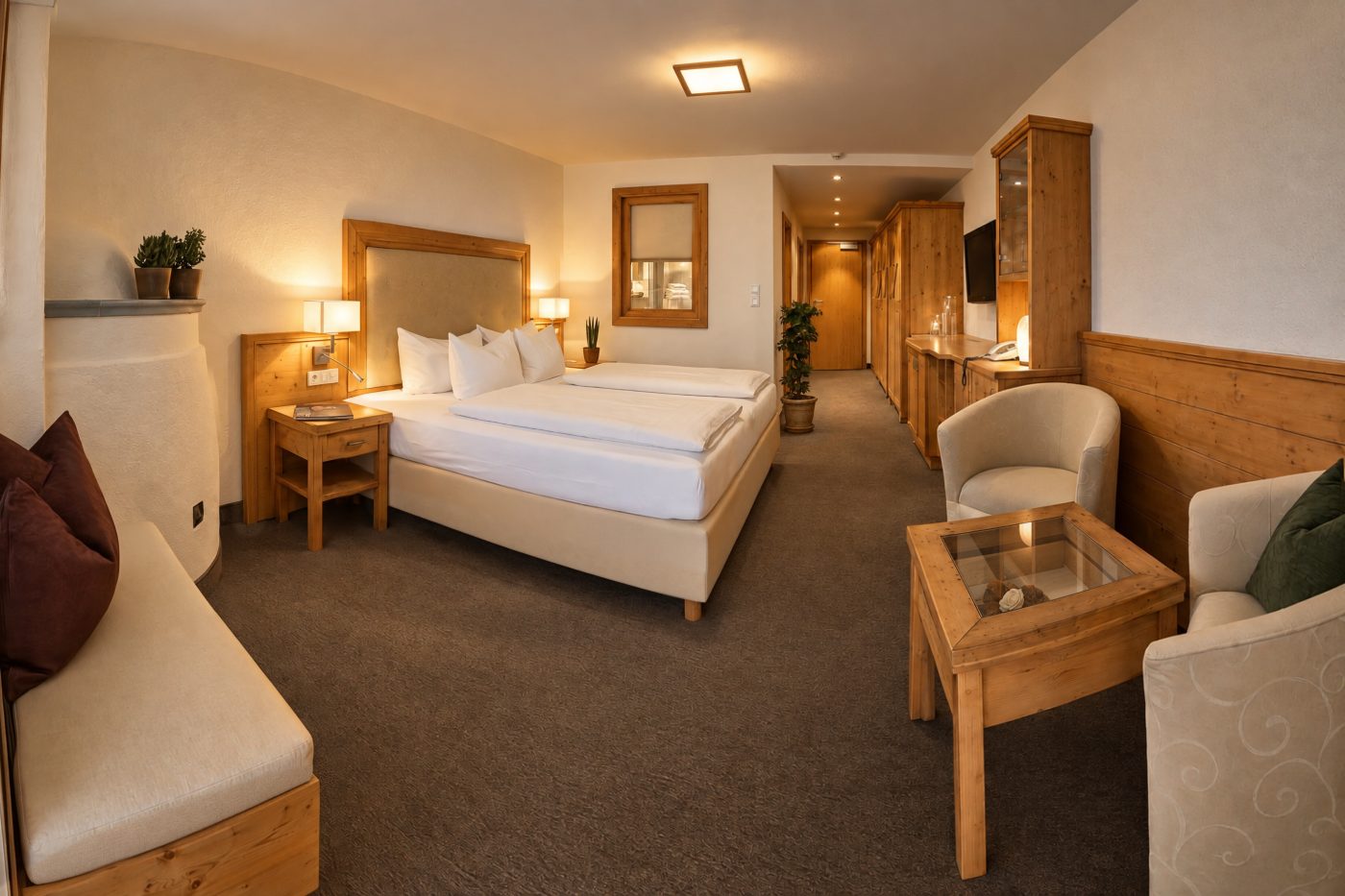 Doppelbett mit gepolstertem Kopfteil, Sitzecke mit zwei Sesseln und Flur mit Kleiderschrank in der Suite Maria Theresia des Hotels DreiSonnen in Serfaus