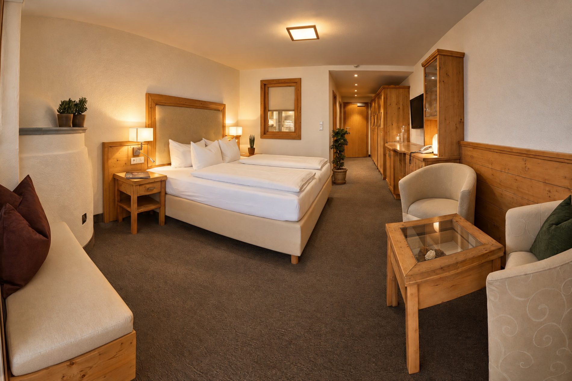 Doppelbett mit gepolstertem Kopfteil, Sitzecke mit zwei Sesseln und Flur mit Kleiderschrank in der Suite Maria Theresia des Hotels DreiSonnen in Serfaus