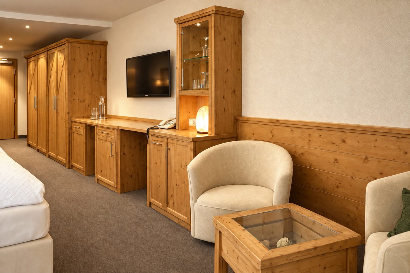 Schreibtisch mit TV, Vitrine und Kleiderschrank aus Holz neben der Sitzecke in der Suite Maria Theresia des Hotels DreiSonnen in Serfaus