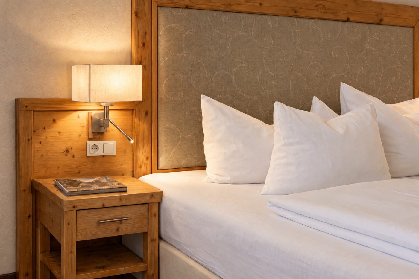Nachttisch mit Leselampe neben dem gepolsterten Kopfteil in der Suite Maria Theresia des Hotels DreiSonnen in Serfaus