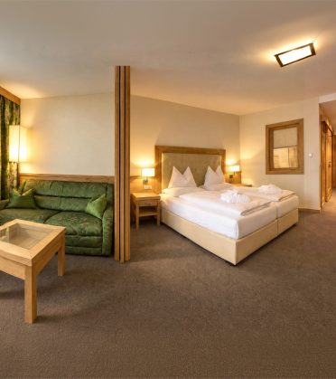 Zimmer Marlene im Hotel DreiSonnen in Serfaus mit Doppelbett, grünem Sofa, Sessel und Blick in den Flur