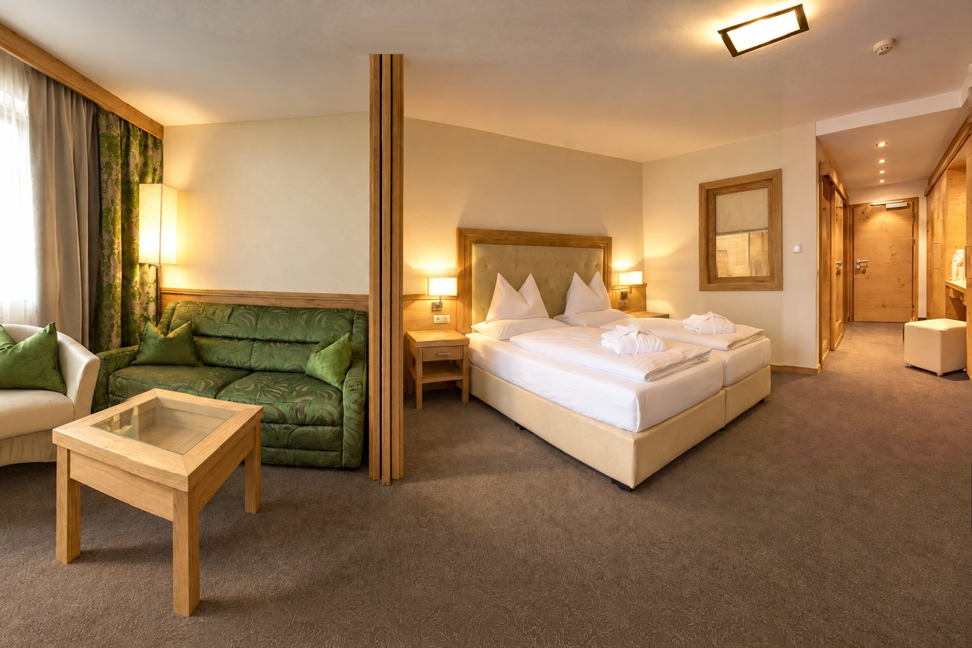 Doppelbett, grünes Sofa und Sitzecke am Fenster im Zimmer Marlene des Hotels DreiSonnen in Serfaus