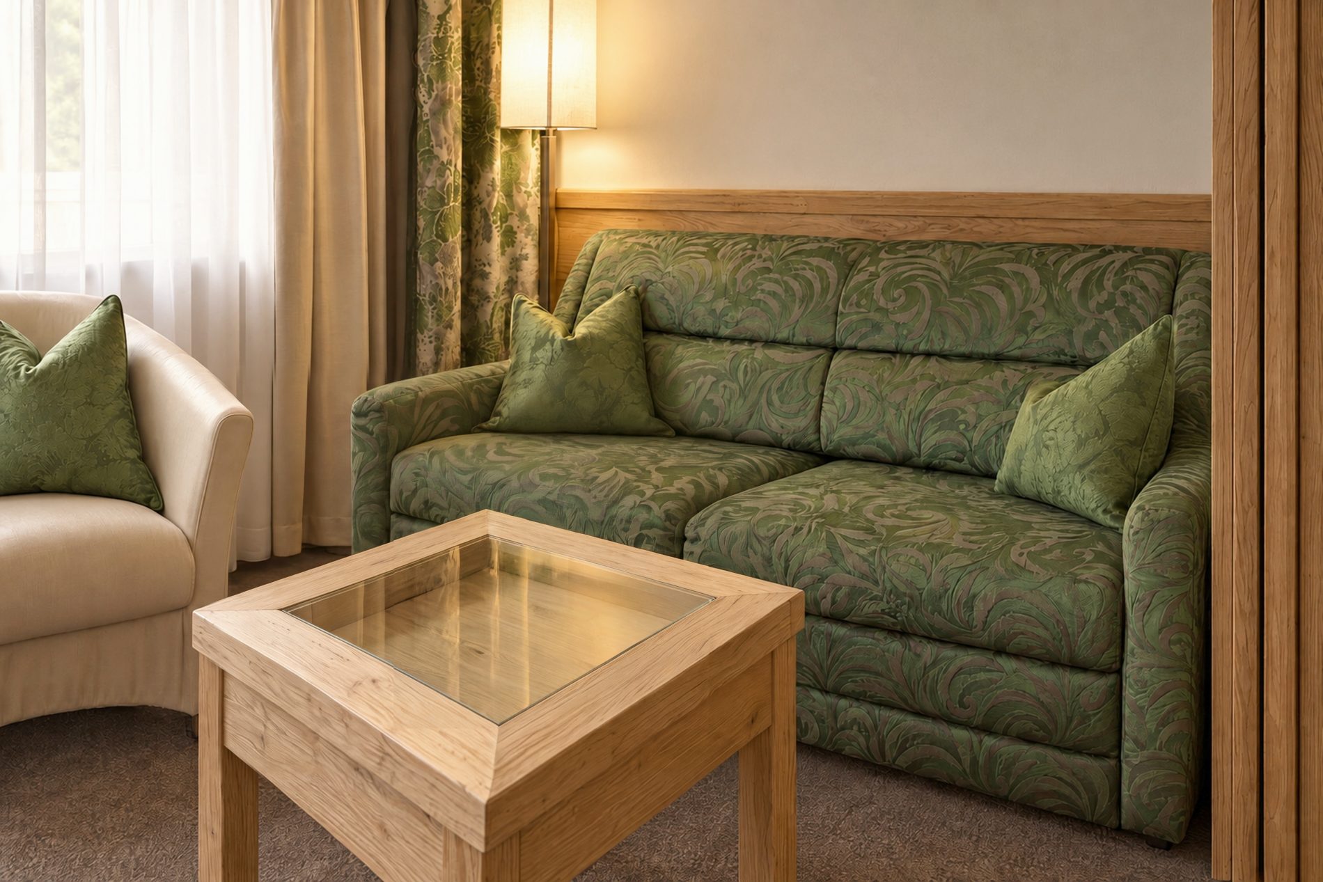 Grünes Sofa mit Sessel und Couchtisch mit Kerzen am Fenster im Zimmer Marlene des Hotels DreiSonnen in Serfaus