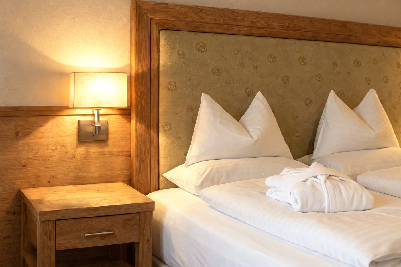 Nachttisch mit Pflanze und Leselampe neben dem gepolsterten Kopfteil im Zimmer Marlene des Hotels DreiSonnen in Serfaus