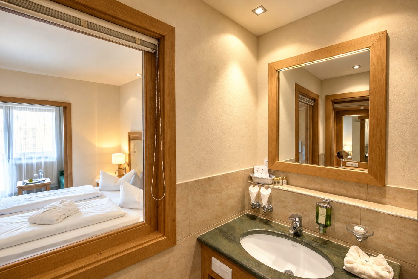 Badezimmer im Zimmer Marlene des Hotels DreiSonnen in Serfaus mit Waschtisch, Spiegel und Fenster zum Schlafbereich