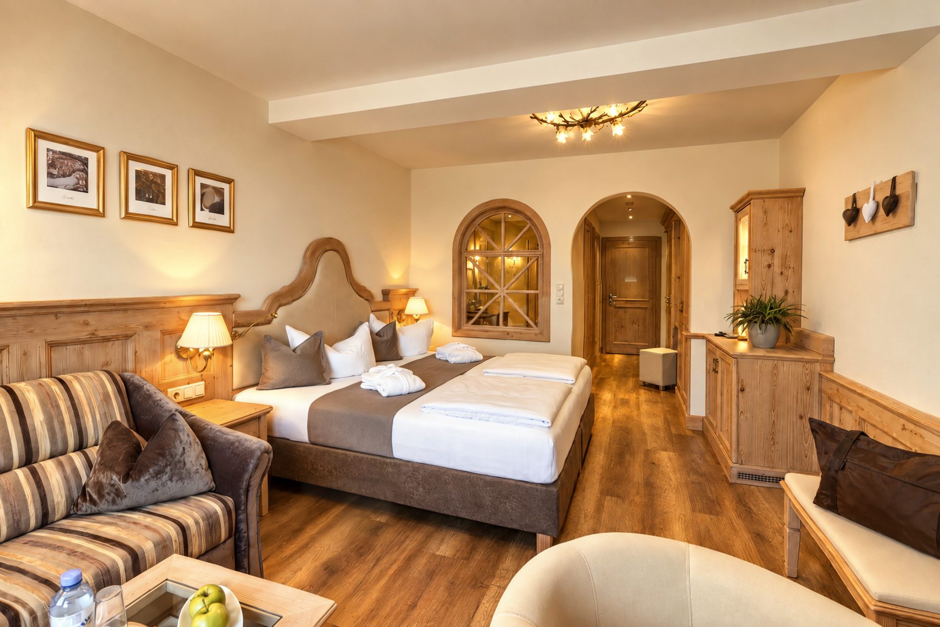 Gestreiftes Sofa, Doppelbett mit geschwungenem Kopfteil und Blick zum Eingang durch den Rundbogen in der Suite Schönbrunn des Hotels DreiSonnen in Serfaus