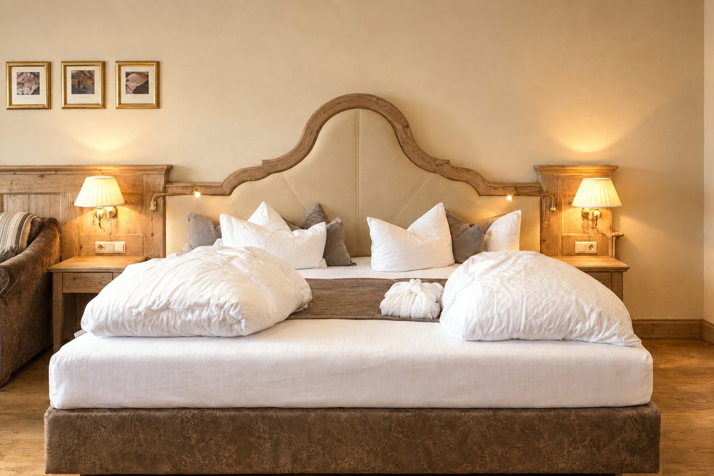 Doppelbett mit geschwungenem Kopfteil, Kunstdrucken und Sofa in der Suite Schönbrunn des Hotels DreiSonnen in Serfaus