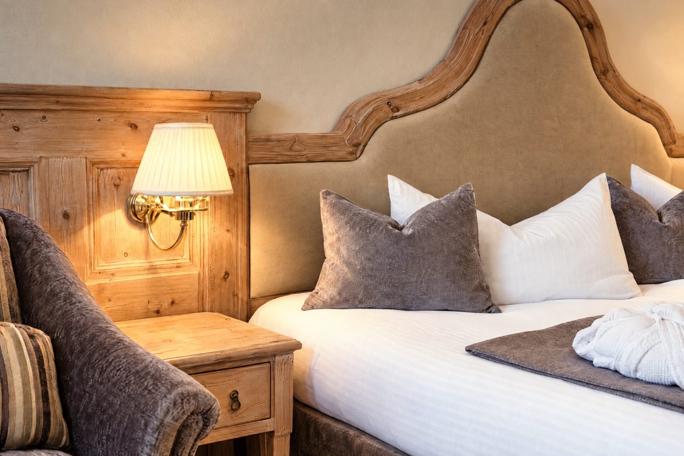 Nachttisch mit Wandleuchte neben dem geschwungenen Kopfteil in der Suite Schönbrunn des Hotels DreiSonnen in Serfaus