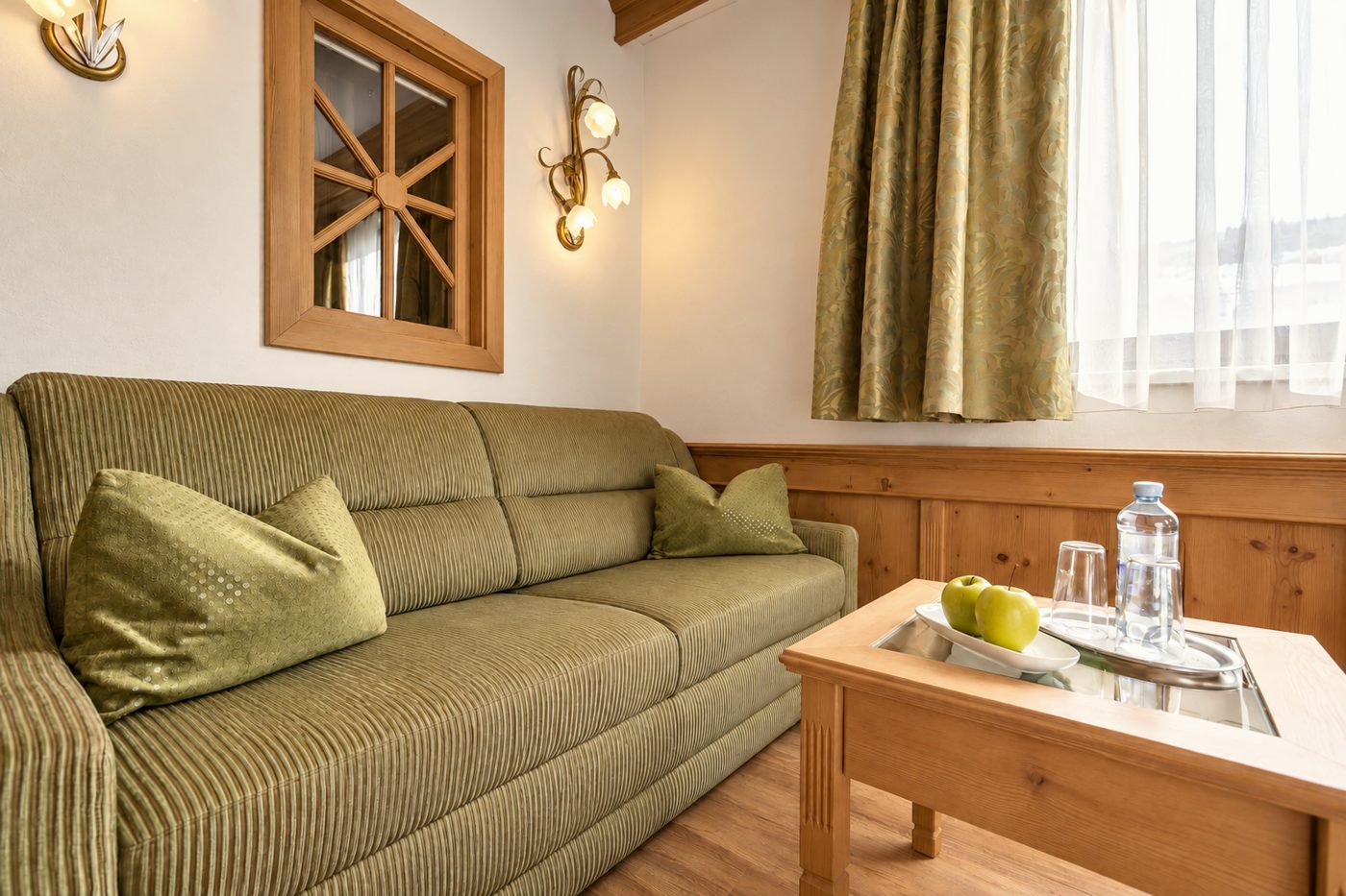 Grünes Sofa mit Couchtisch unter dem Sprossenfenster in der Suite Schönbrunn des Hotels DreiSonnen in Serfaus