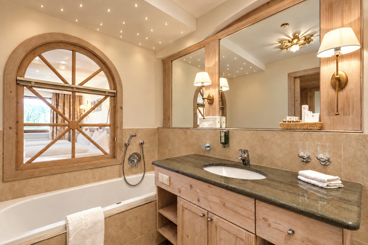 Badezimmer in der Suite Schönbrunn des Hotels DreiSonnen in Serfaus mit Waschtisch, Spiegel, Badewanne und Rundbogenfenster