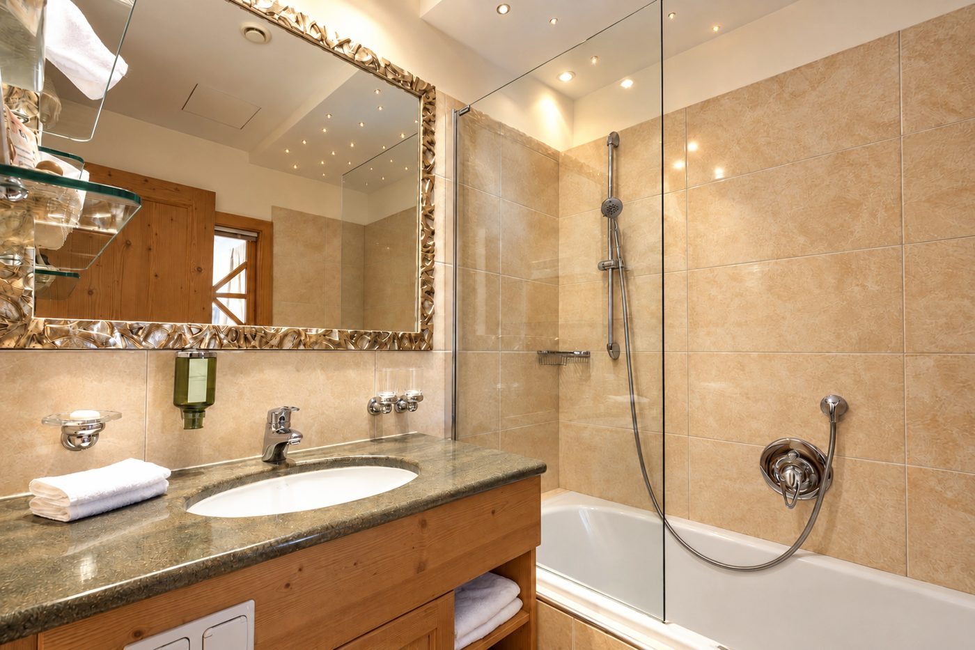Zweites Badezimmer in der Suite Schönbrunn des Hotels DreiSonnen in Serfaus mit Waschtisch, Spiegel und Badewanne mit Duschwand
