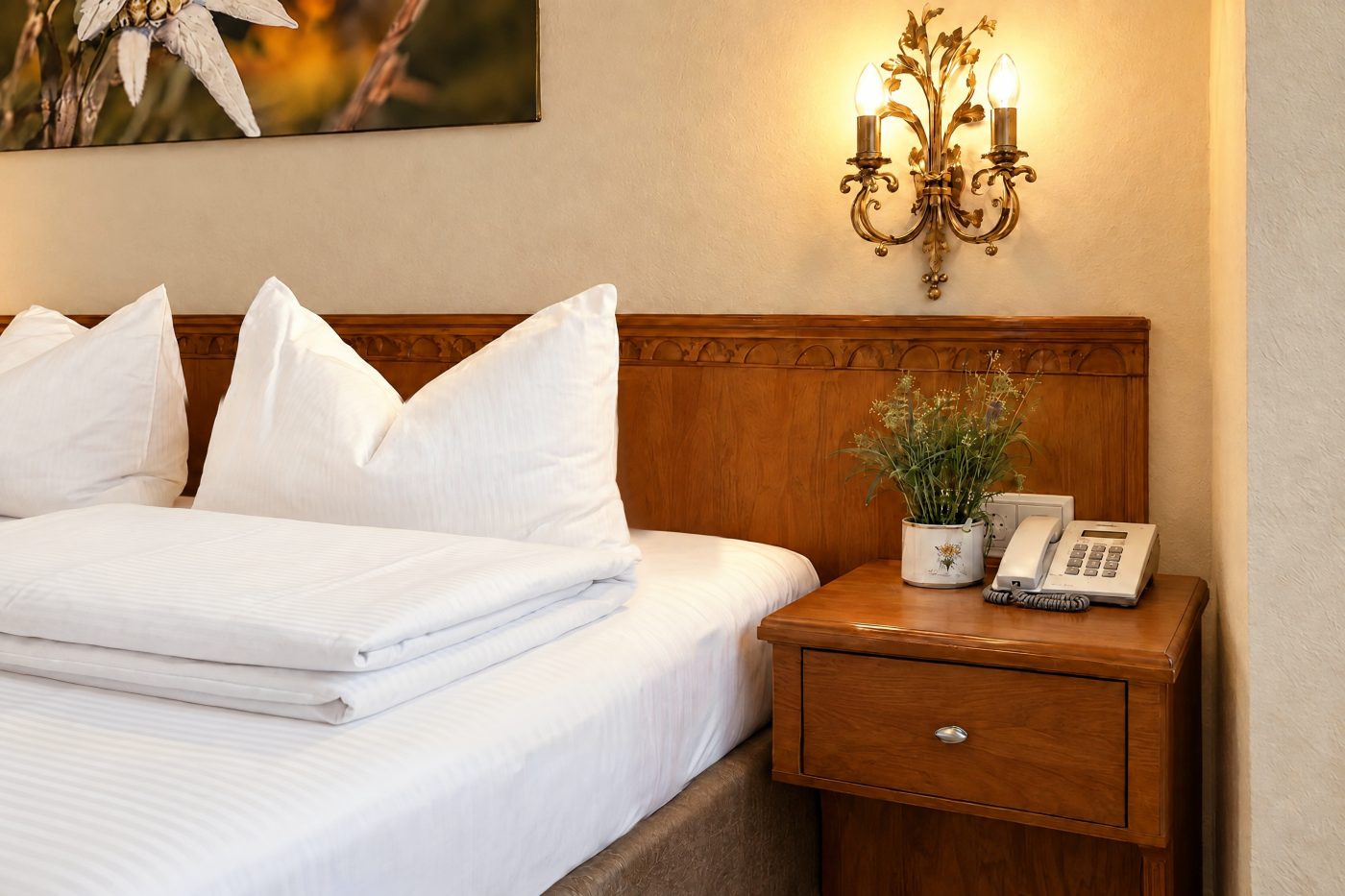 Bedside table with flowerpot and wall light next to the bed in the room Valentina at Hotel DreiSonnen in Serfaus