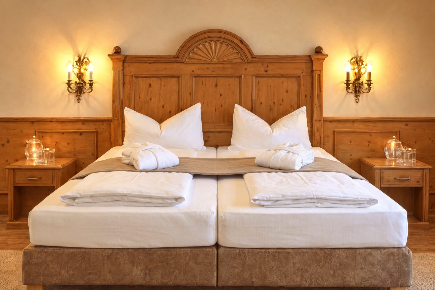 Doppelbett mit geschnitztem Kopfteil aus Holz, Nachttischen und Wandleuchten im Zimmer Viktoria des Hotels DreiSonnen in Serfaus