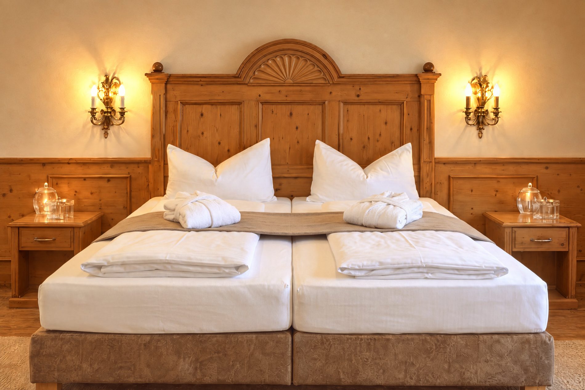 Doppelbett mit geschnitztem Kopfteil aus Holz, Nachttischen und Wandleuchten im Zimmer Viktoria des Hotels DreiSonnen in Serfaus