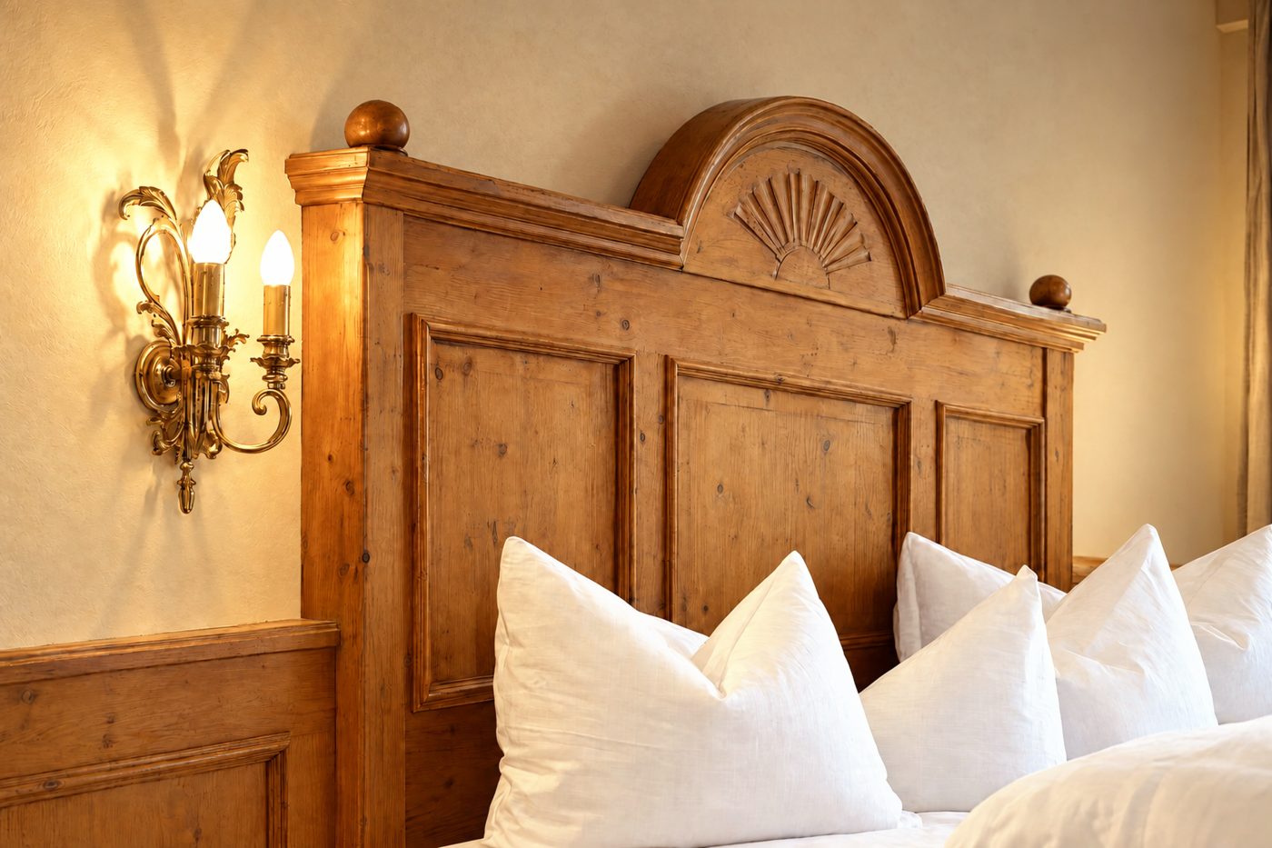 Geschnitztes Kopfteil aus Holz mit Muschelmotiv und Wandleuchte im Zimmer Viktoria des Hotels DreiSonnen in Serfaus