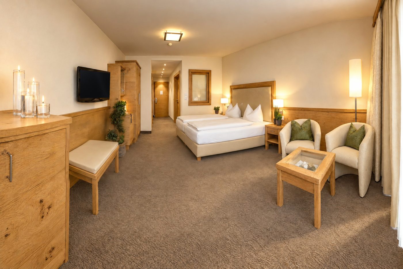 Doppelbett, zwei Sessel mit Couchtisch und TV in einem vergleichbaren Doppelzimmer vom Typ des Zimmers Viktoria im Hotel DreiSonnen in Serfaus