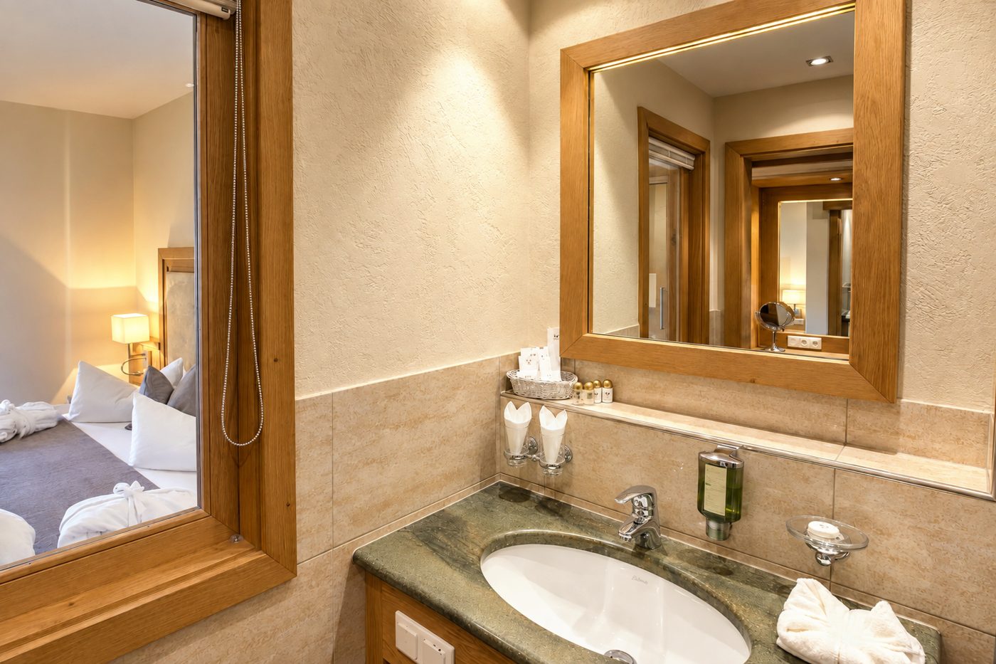 Badezimmer mit Waschtisch, Spiegel und Innenfenster zum Schlafbereich in einem vergleichbaren Doppelzimmer vom Typ des Zimmers Viktoria im Hotel DreiSonnen in Serfaus