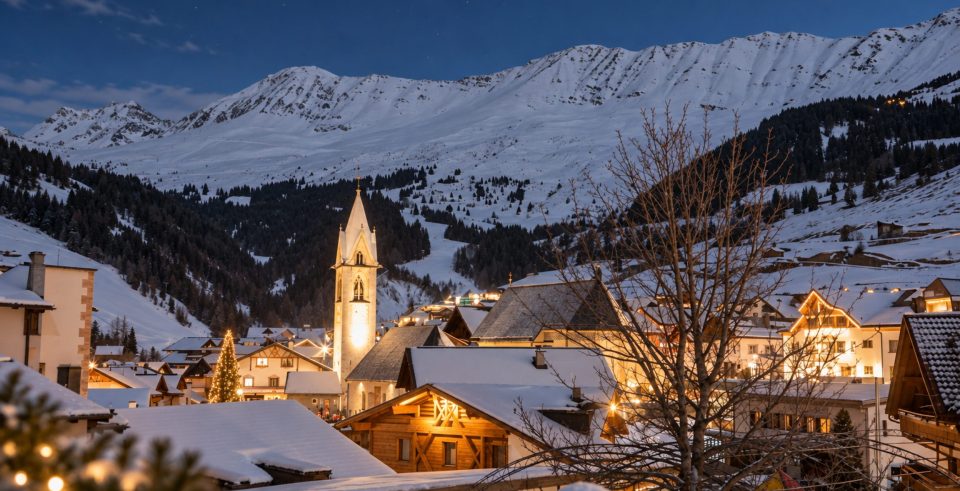 Verschneites Bergdorf mit Kirchturm und erleuchteten Häusern am Abend