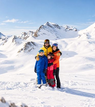 Familie in Skikleidung im Schnee vor verschneiten Bergen