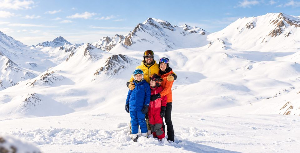 Familie in Skikleidung im Schnee vor verschneiten Bergen