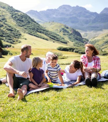 Familie mit drei Kindern beim Picknick auf einer Almwiese