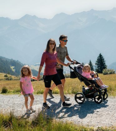 Eltern mit Kinderwagen und kleiner Tochter auf einem Schotterweg in den Bergen