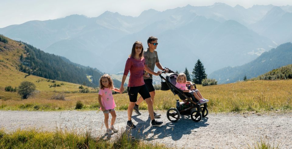 Eltern mit Kinderwagen und kleiner Tochter auf einem Schotterweg in den Bergen