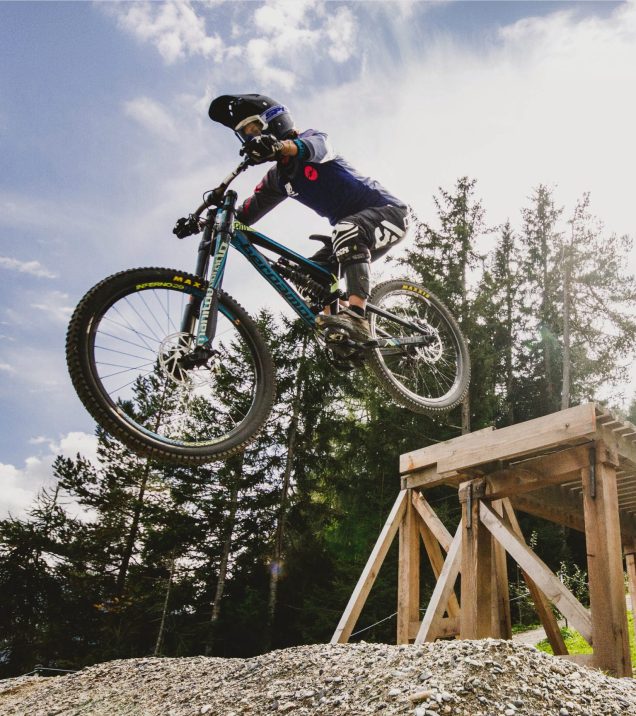 Ein Biker springt im Bikepark über eine Holzrampe.