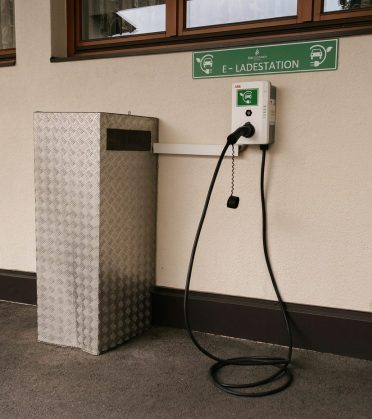 EV charging point on the wall of Hotel DreiSonnen with a charging cable and a green sign „E-Ladestation"