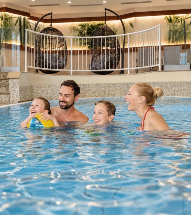 Eine Familie spielt mit einem Wasserball im Innenpool des Hotel DreiSonnen in Serfaus.