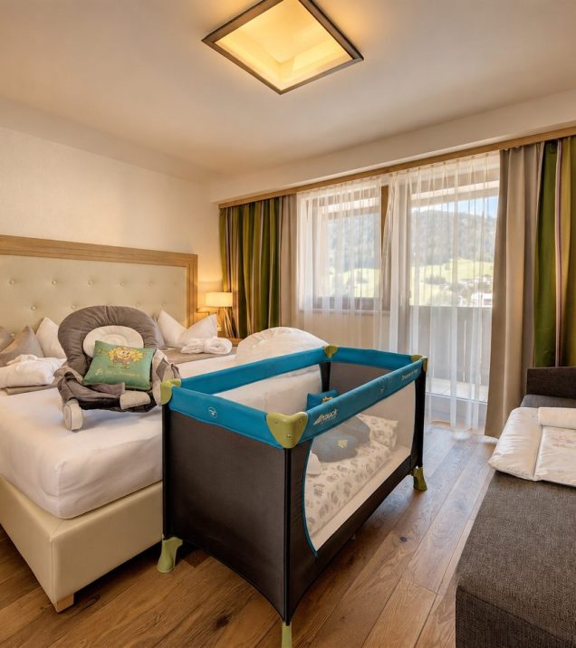 Familienzimmer mit Doppelbett, Babywippe und blauem Reisebett vor den Balkonfenstern