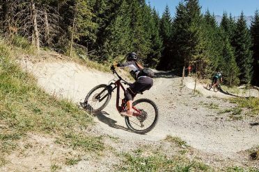 Eine Bikerin fährt durch eine Schotterkurve auf einem Flowtrail im Wald.