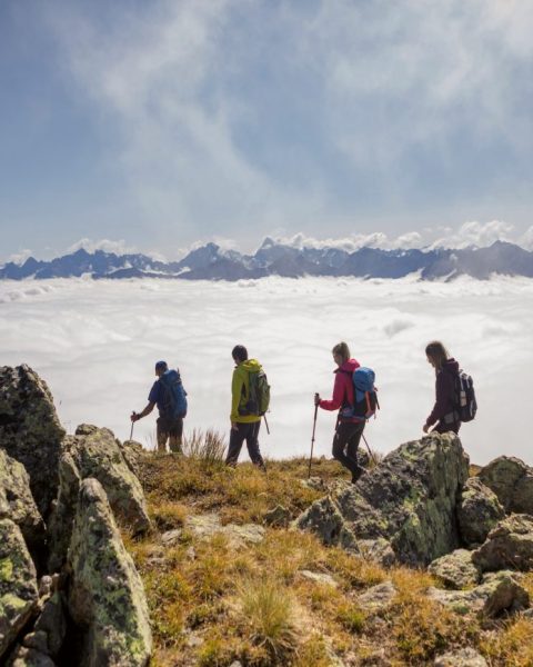 Four hikers on a rocky ridge above a sea of cloud.
